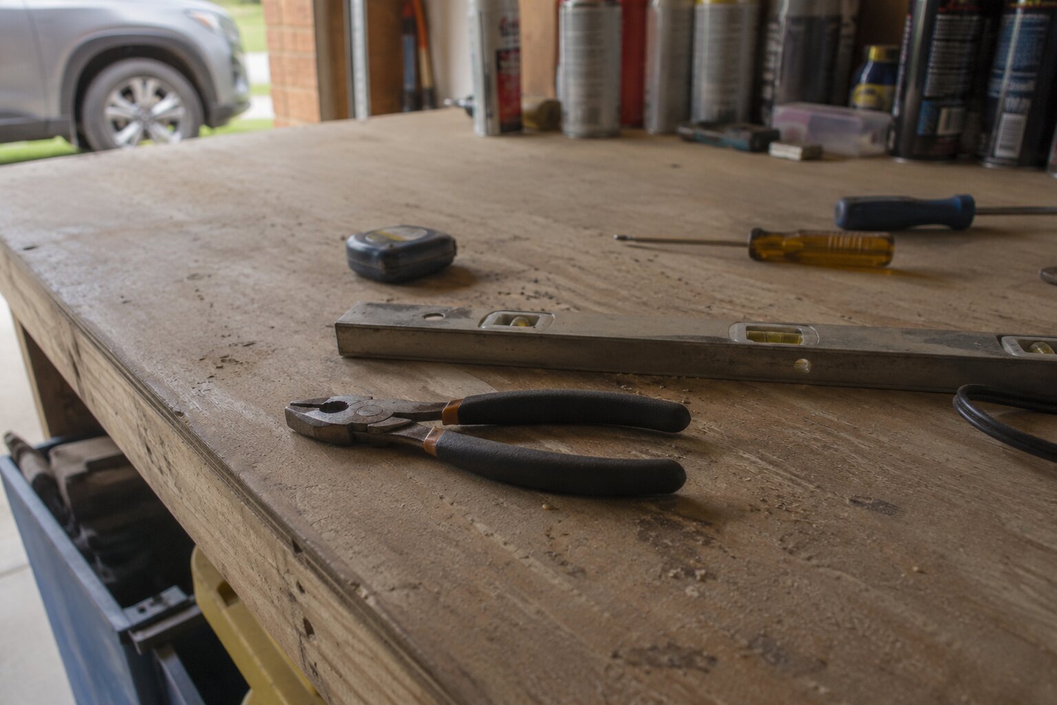 A worn garage workbench with pliers, a level, a tape measure, and screwdrivers.